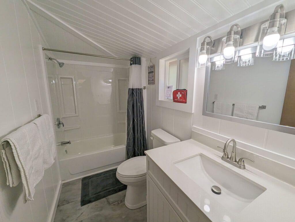 A bright, modern bathroom with a white vanity, sleek fixtures, and a shower-tub combo with a white shower curtain. White paneling and clean lines create a fresh and inviting space.